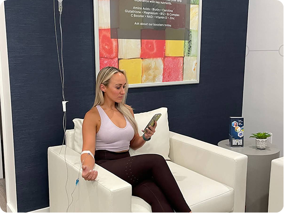 A woman receiving drip treatment while sitting on a comfortable chair looking at her phone.